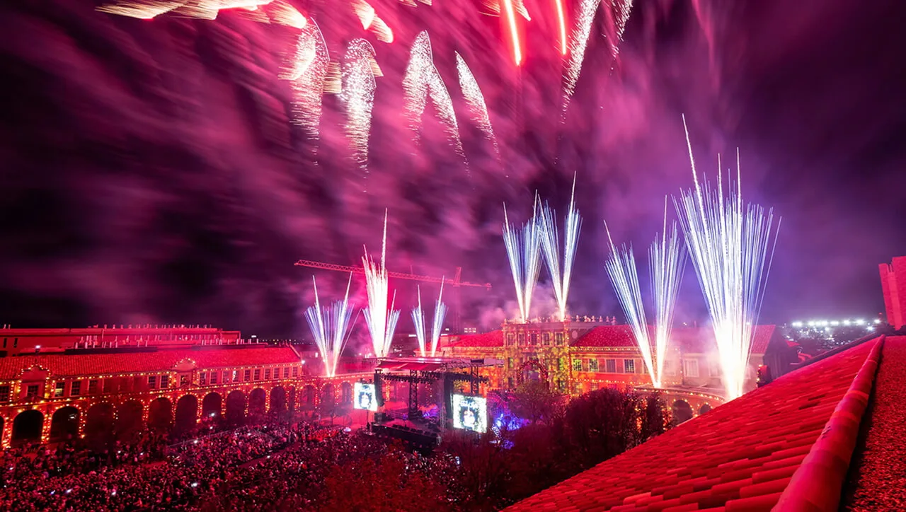 Fireworks over a crowd in a campus courtyard lit up in red