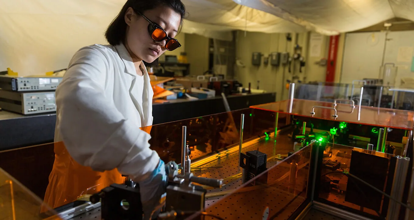 A researcher in safety glasses adjusting laser equipment in a lab