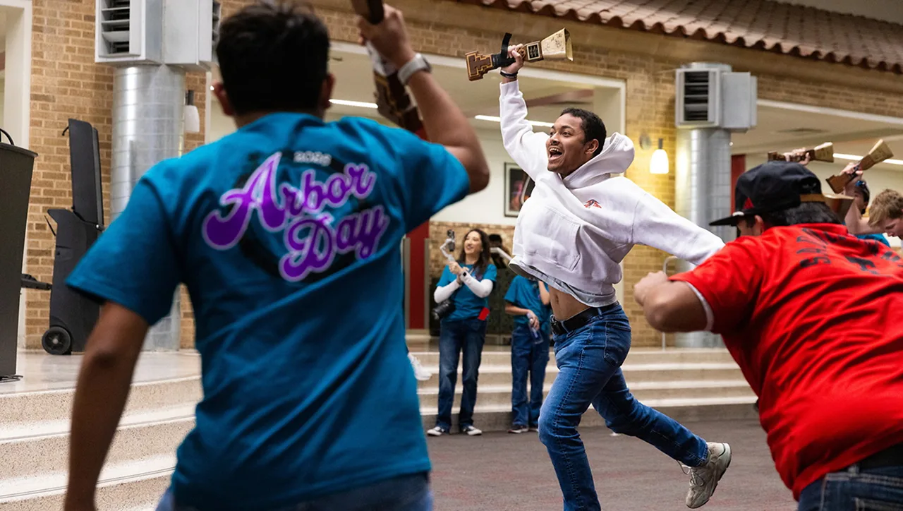 Students playfully battling with foam weapons during an Arbor Day event on campus